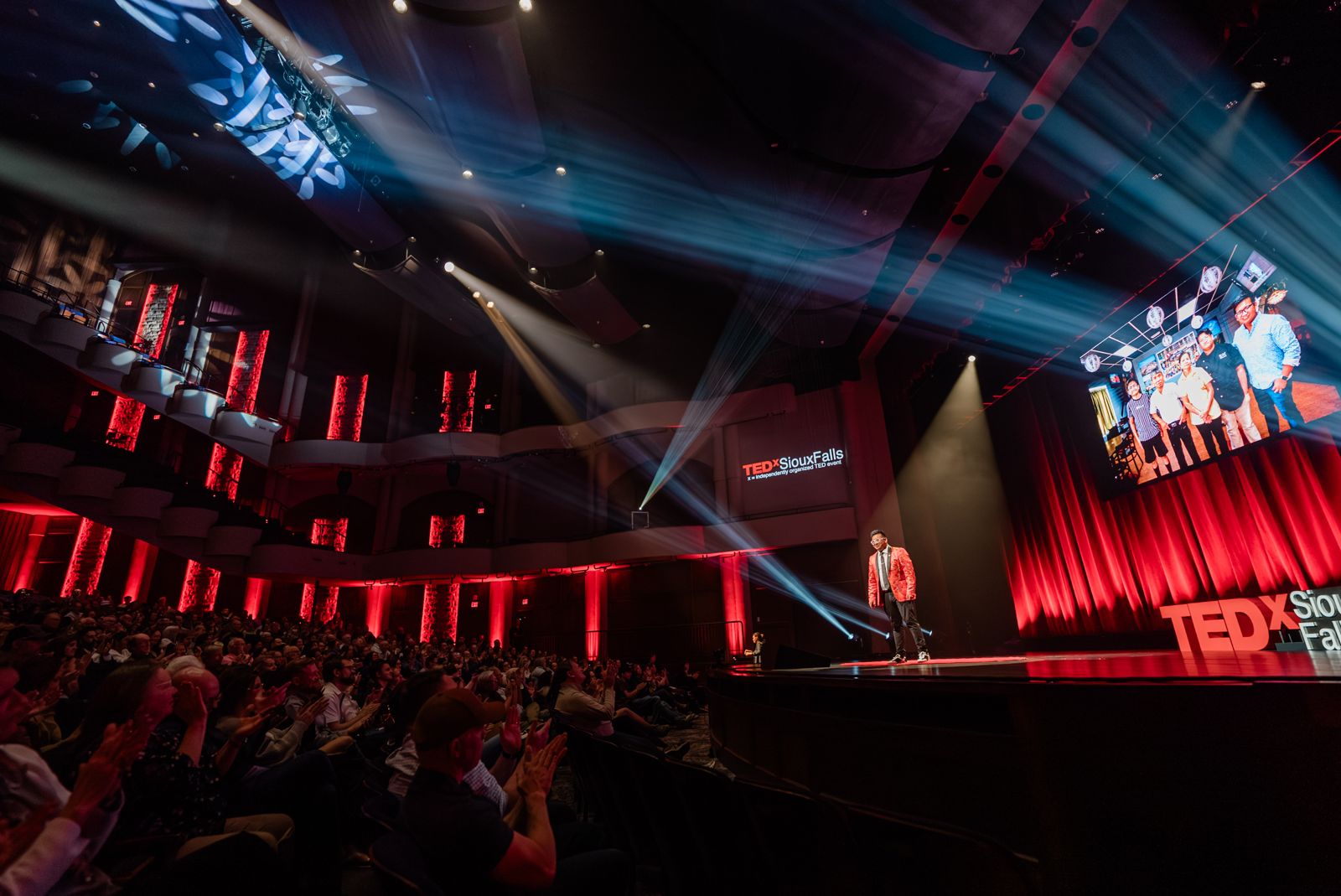 Vince on stage at TEDx Sioux Falls in front of a full, applauding theater, with a photo of his family's restaurant on the big screen