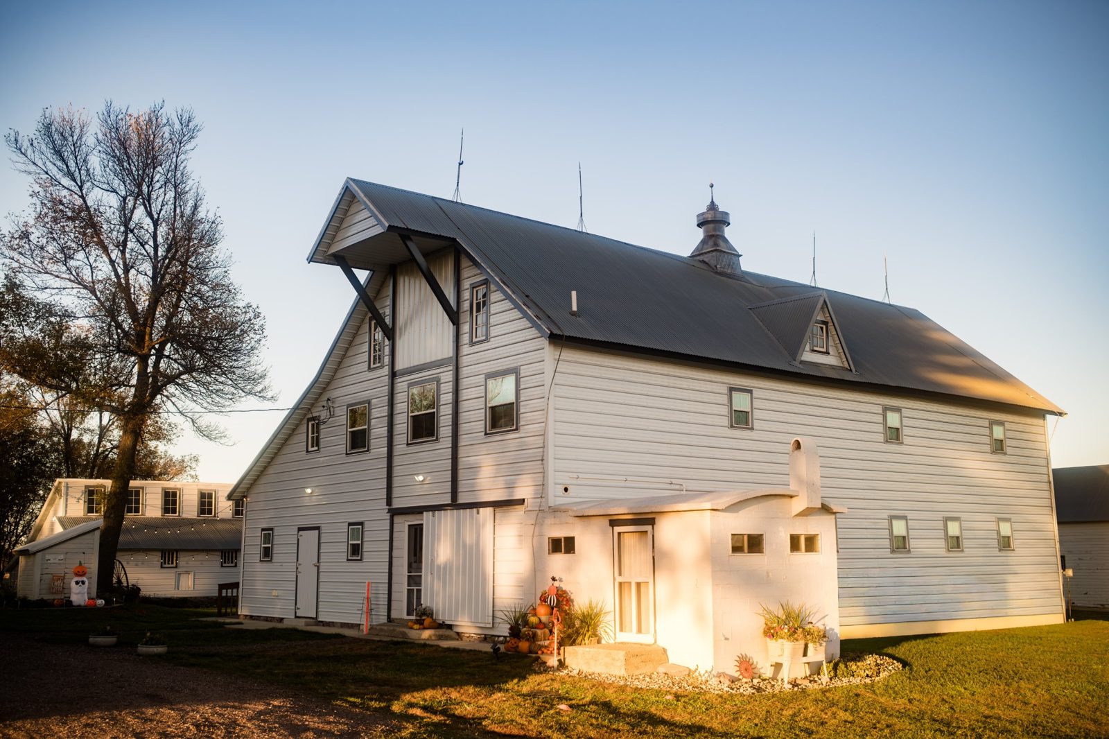 A white barn at the Kelly Family Homestead near Crooks at sunset, with pumpkins by the door
